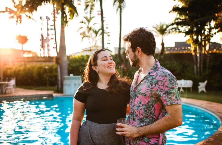 A couple smiling happily by a pool during sunset, capturing a romantic summer moment.