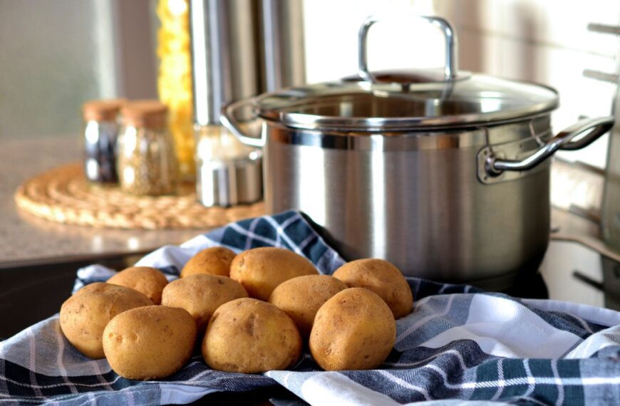 Fresh potatoes on cloth beside a stainless pot, ready for cooking in a modern kitchen.