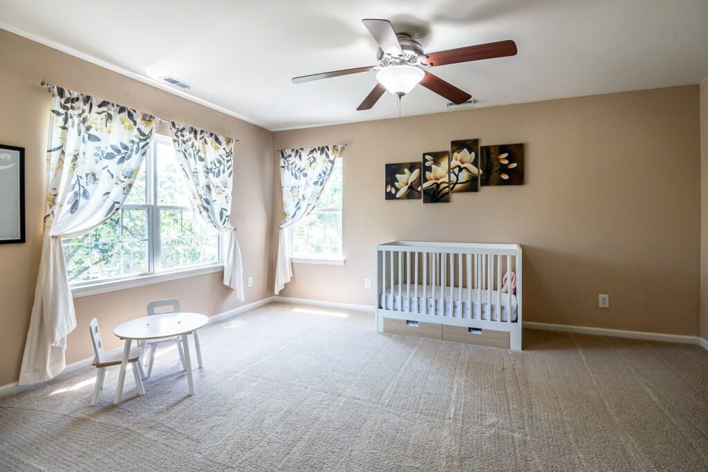 A spacious nursery room with a crib, white table and chair set, and floral curtains under natural light.