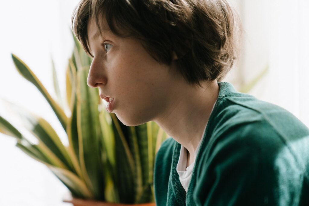 Profile portrait of a thoughtful young teenager indoors with houseplants in the background.