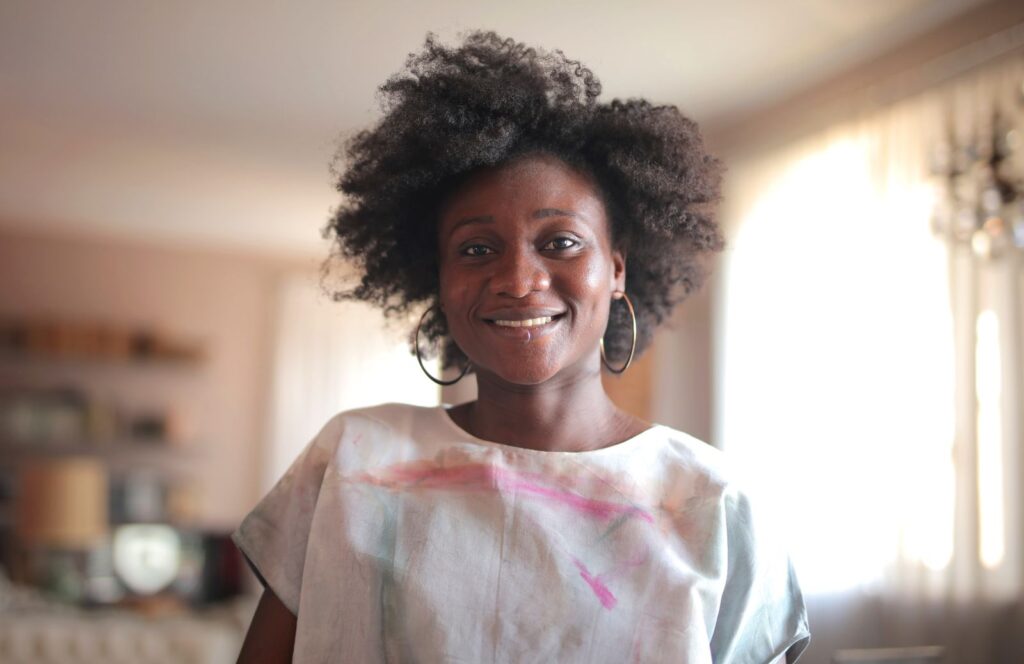 Portrait of a smiling woman with natural afro hair in a cozy indoor setting.