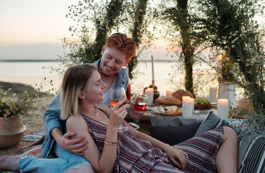 Couple enjoying a romantic outdoor picnic with wine and candles, creating a perfect evening atmosphere.