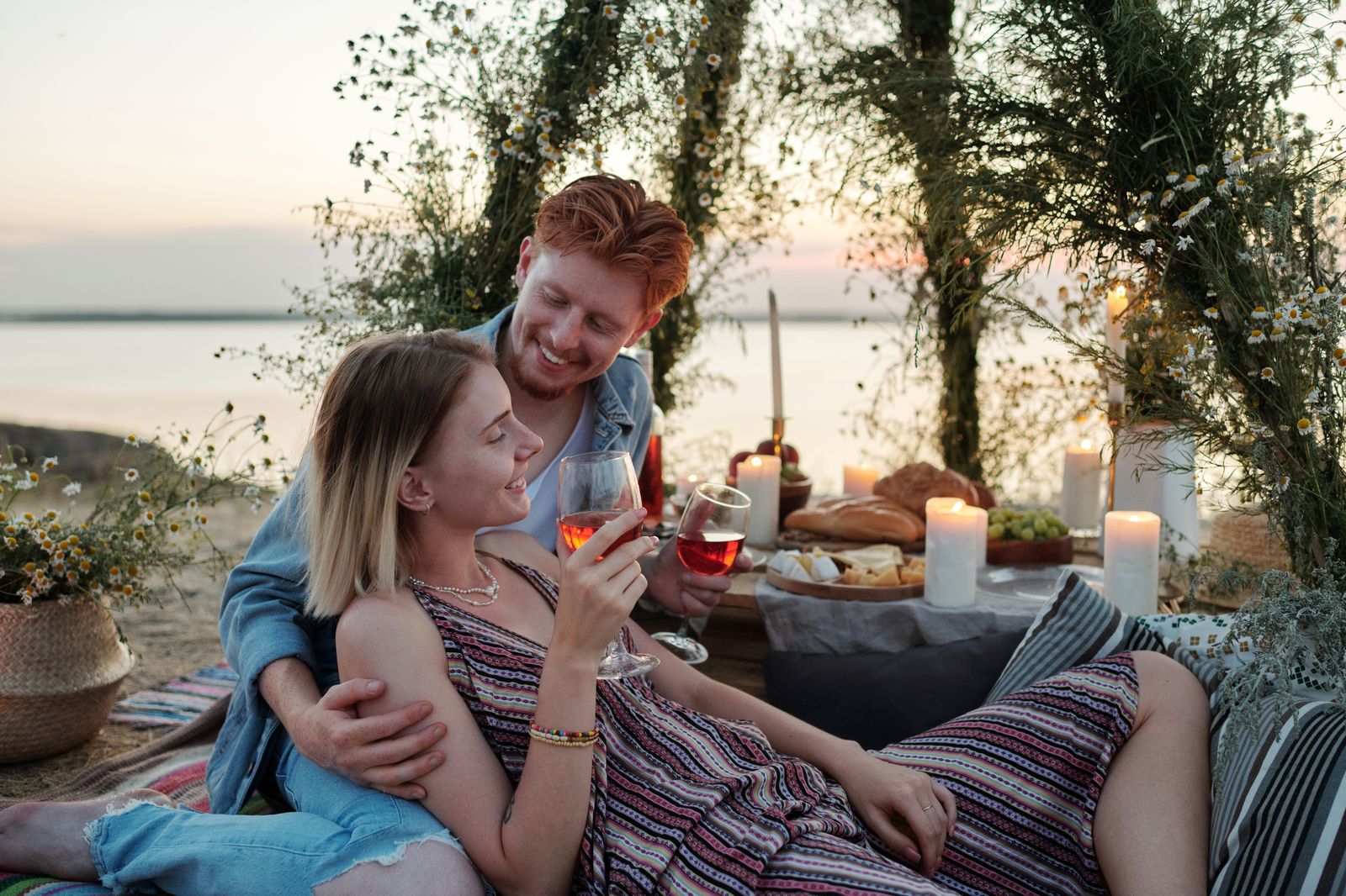 Couple enjoying a romantic outdoor picnic with wine and candles, creating a perfect evening atmosphere.