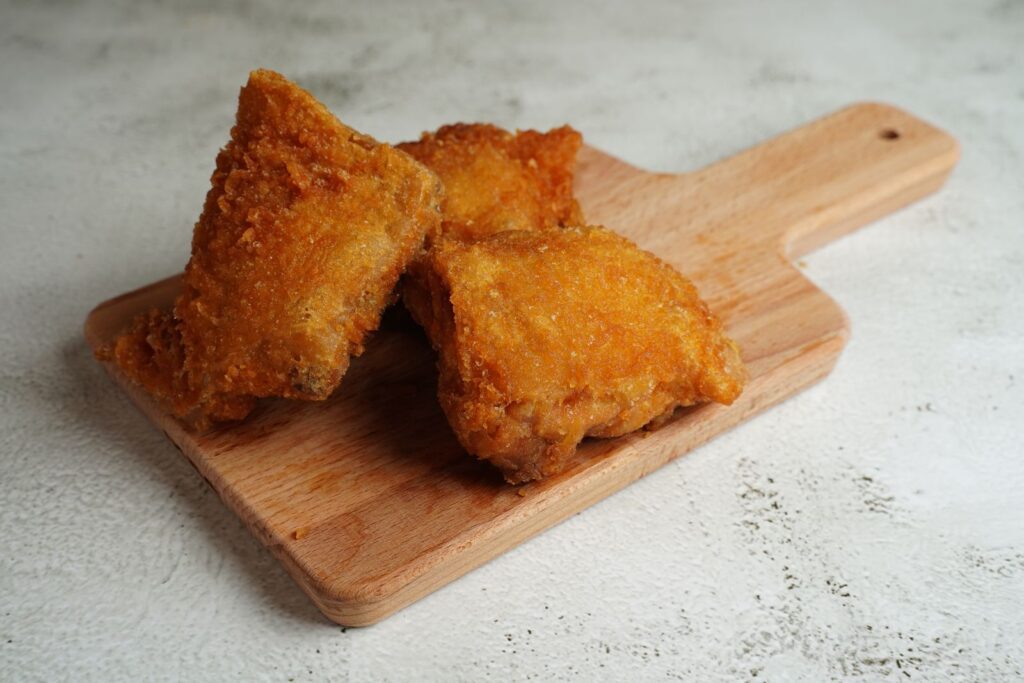 Three pieces of golden brown fried chicken on a wooden cutting board.