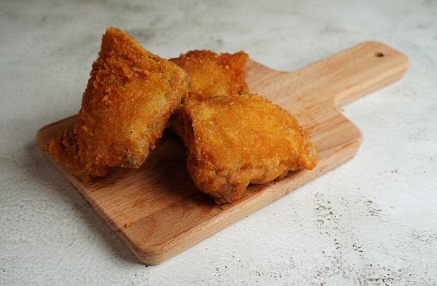 Three pieces of golden brown fried chicken on a wooden cutting board.
