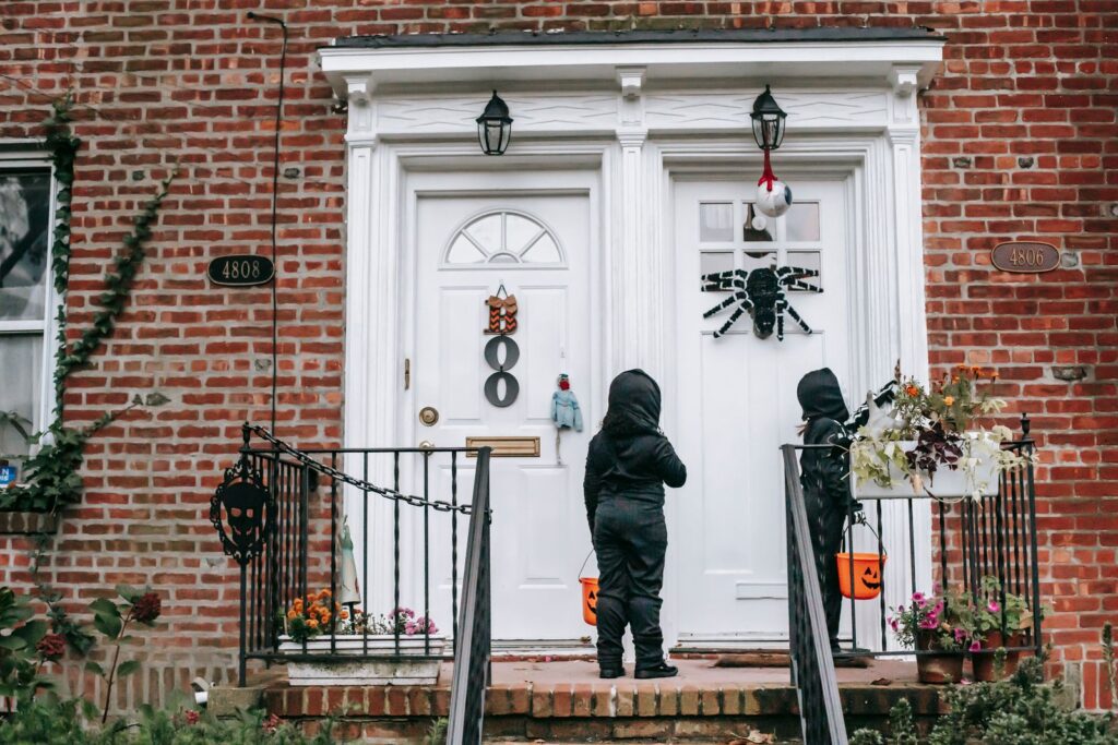 Full length of unrecognizable kids in Halloween costumes with masks standing near house door with buckets in daytime