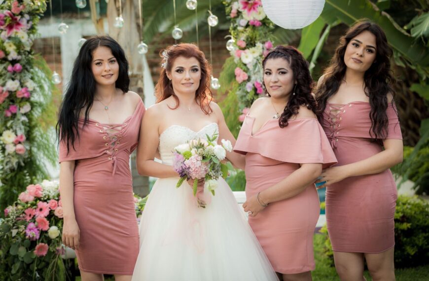 Bride and bridesmaids in pink dresses posing in a lush garden setting with floral decorations.
