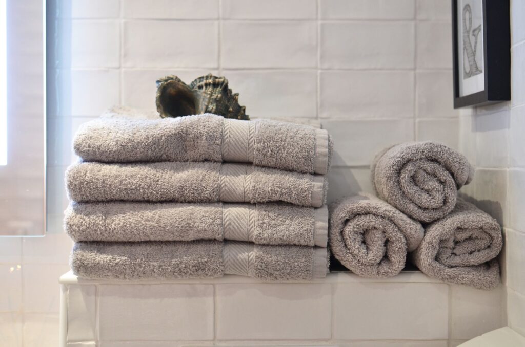 Big shell placed on heap of soft gray towels arranged on shelf near white tiled wall in modern bathroom