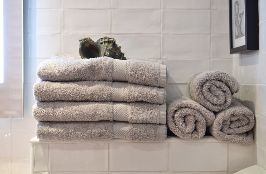 Big shell placed on heap of soft gray towels arranged on shelf near white tiled wall in modern bathroom