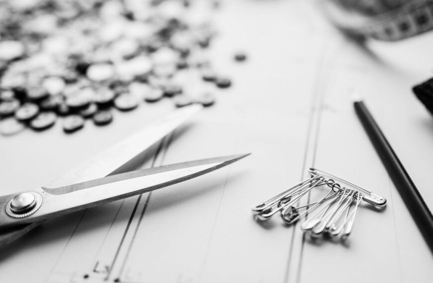 Close-up of scissors, safety pins, and buttons on a worktable in a sewing workshop.