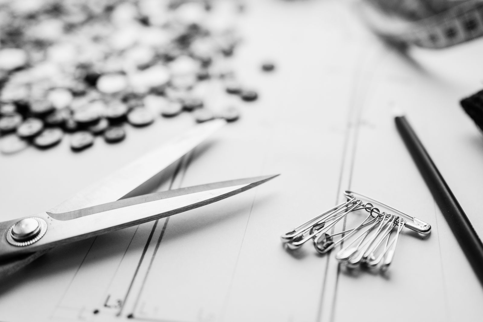 Close-up of scissors, safety pins, and buttons on a worktable in a sewing workshop.