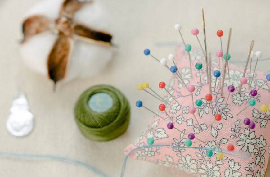 From above colorful pins attached to small pillow placed on table with thread roll and cotton ball in workshop