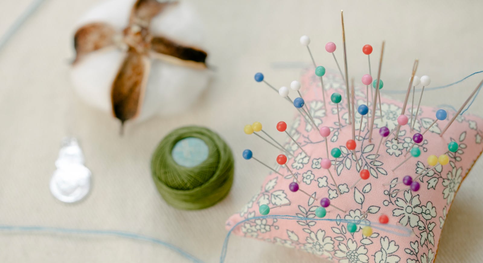 From above colorful pins attached to small pillow placed on table with thread roll and cotton ball in workshop