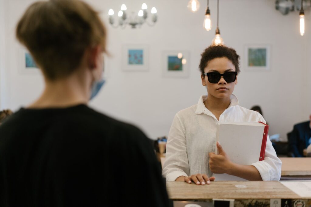 A blind woman confidently navigates a cafe, holding a folder, exhibiting empowerment and independence.