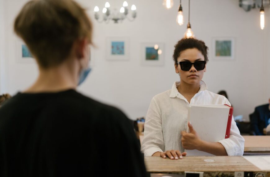 A blind woman confidently navigates a cafe, holding a folder, exhibiting empowerment and independence.