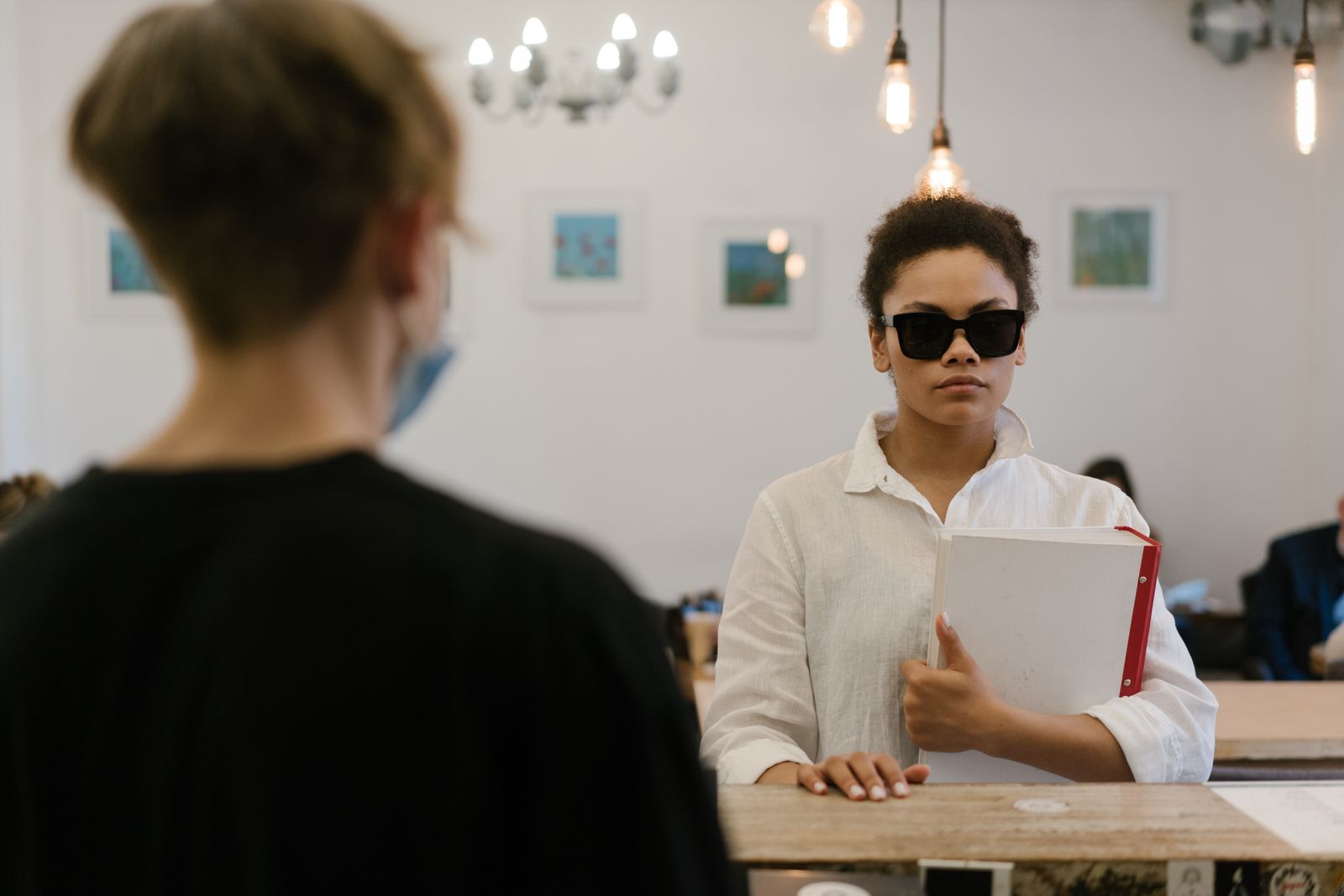 A blind woman confidently navigates a cafe, holding a folder, exhibiting empowerment and independence.