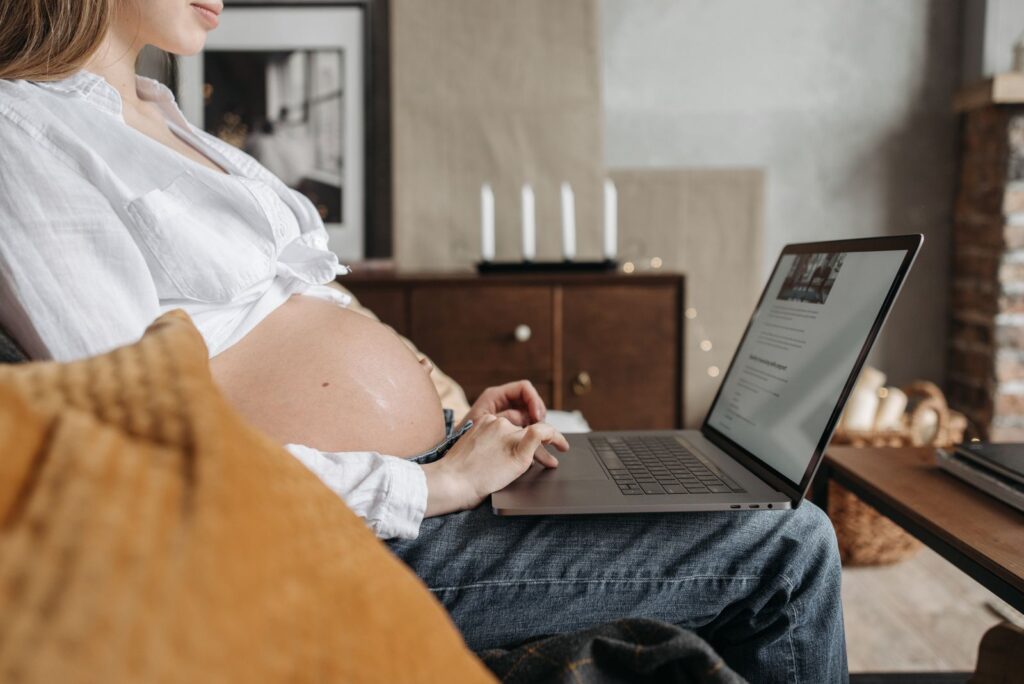 Expectant mother using a laptop while sitting in a cozy home environment, emphasizing remote work during pregnancy.
