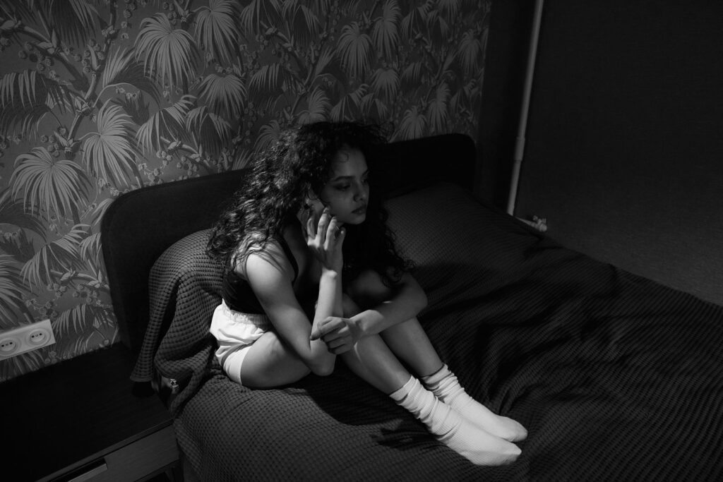 A woman sitting on a bed, deep in thought, in a monochrome setting.