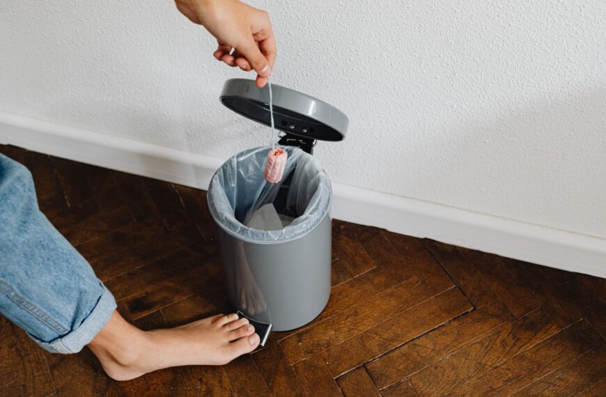 A person disposing a tampon in a trash bin with a foot pedal inside a home setting.