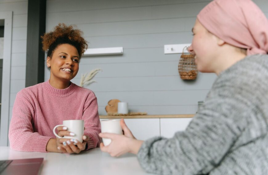 Two women share a joyful coffee moment at home, embodying friendship and warmth.