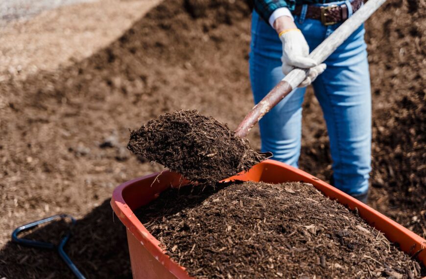 A person shovels compost into a red container, preparing soil for gardening.