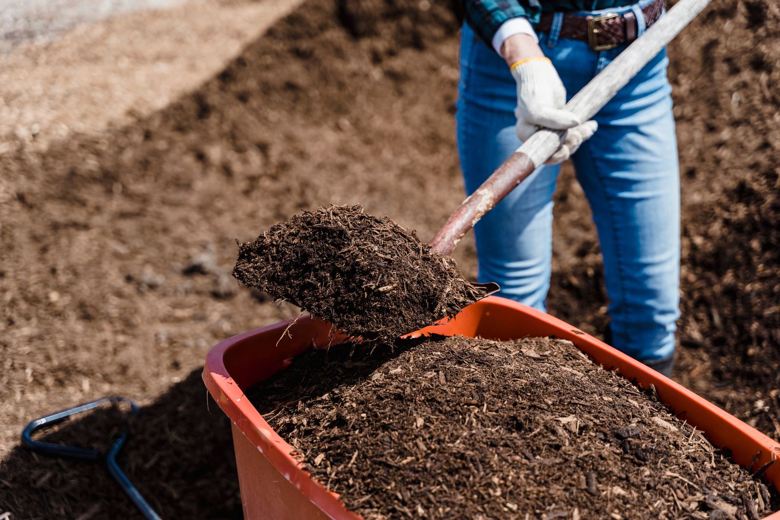 A person shovels compost into a red container, preparing soil for gardening.