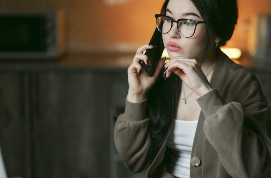 A woman with eyeglasses engaged in a phone call indoors, focused and thoughtful.