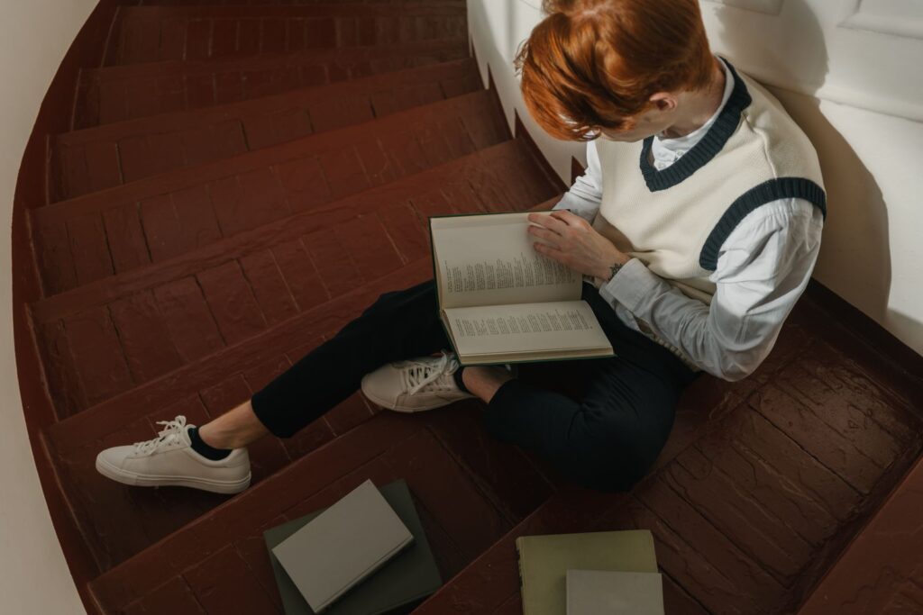 A young man reading a book while sitting on a rustic wooden staircase, exuding concentration and tranquility.