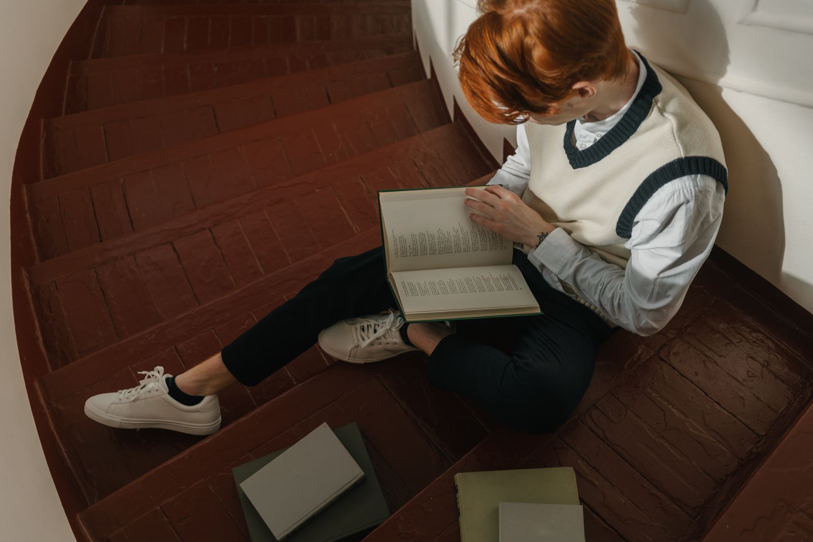 A young man reading a book while sitting on a rustic wooden staircase, exuding concentration and tranquility.