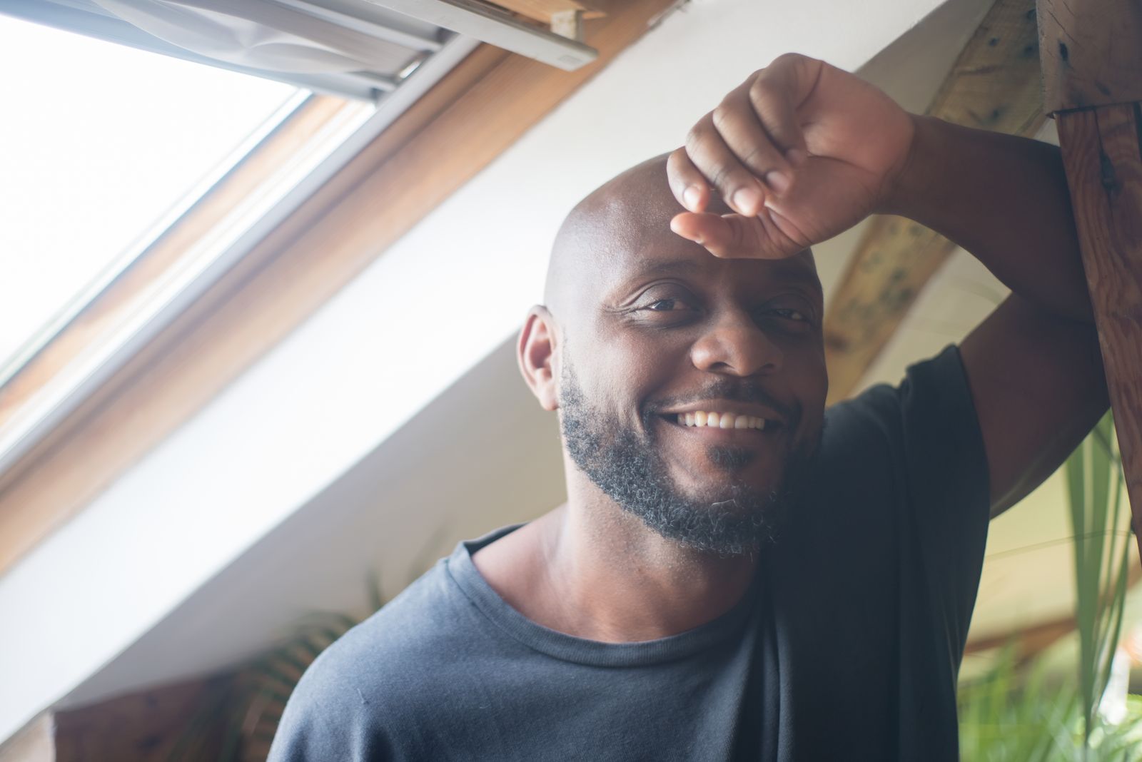 Portrait of a smiling man relaxing by a skylight, enjoying natural light indoors.