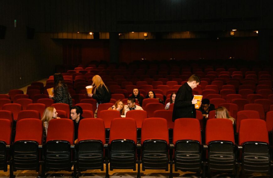 Group of people enjoying a movie with snacks in a cinema with red seats.