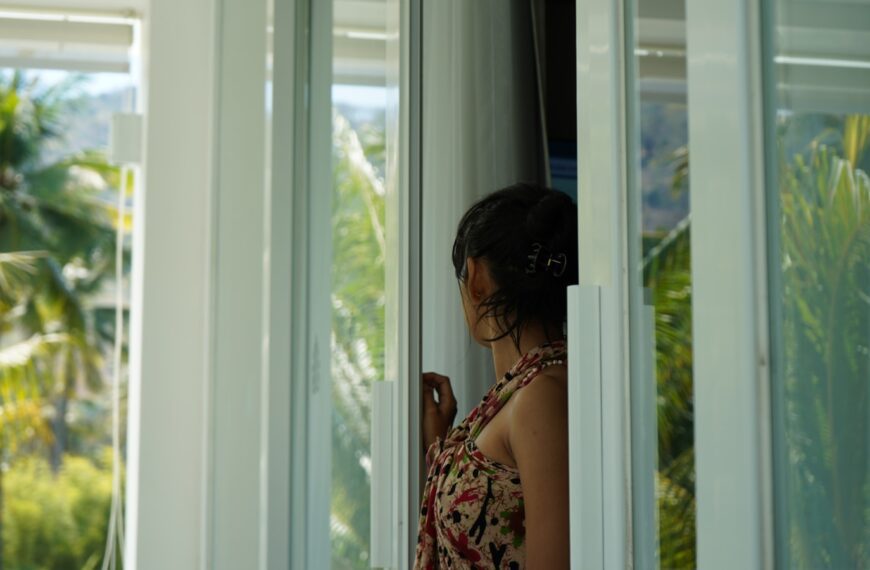 A woman looking out of a window at palm trees