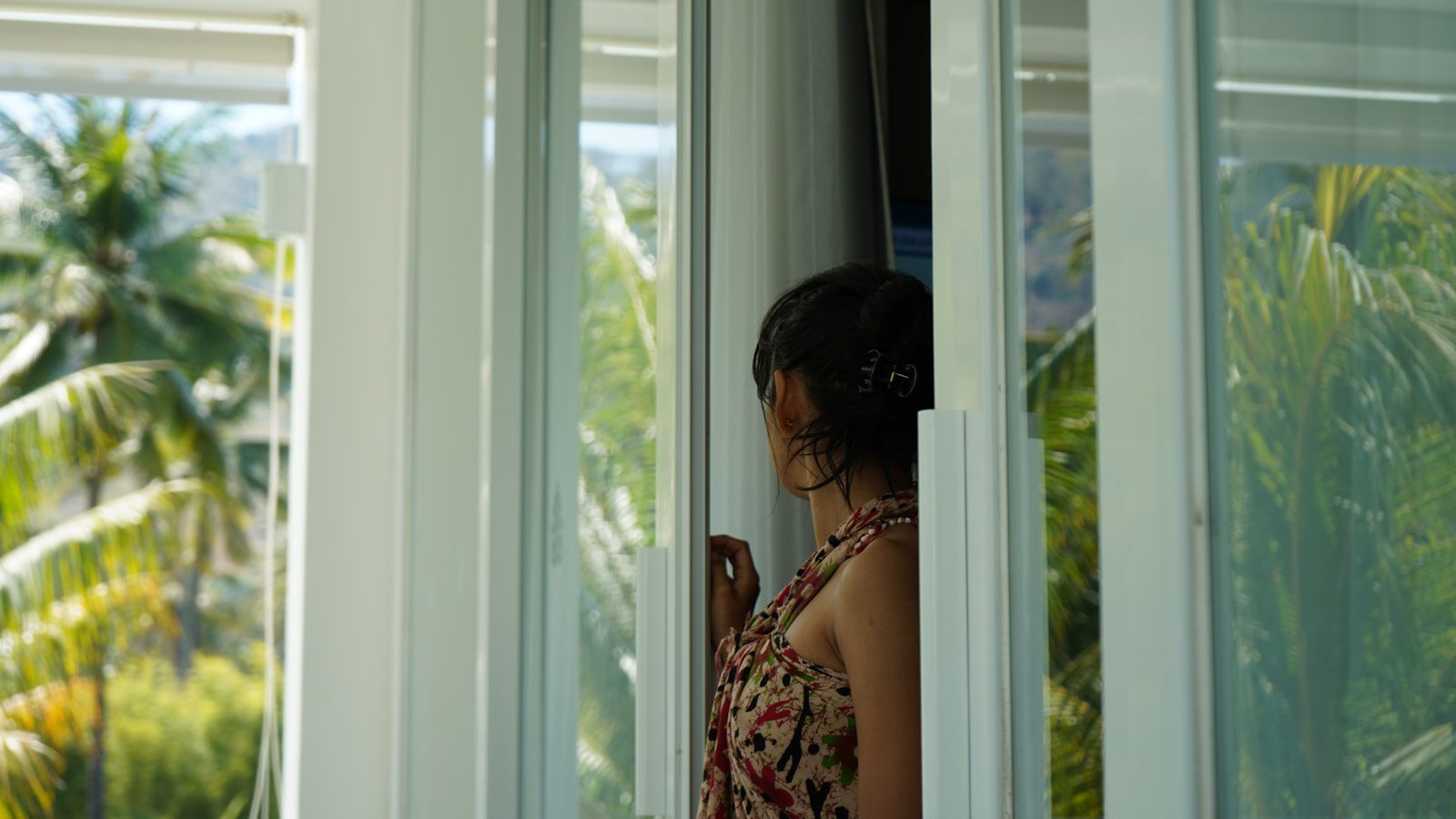 A woman looking out of a window at palm trees