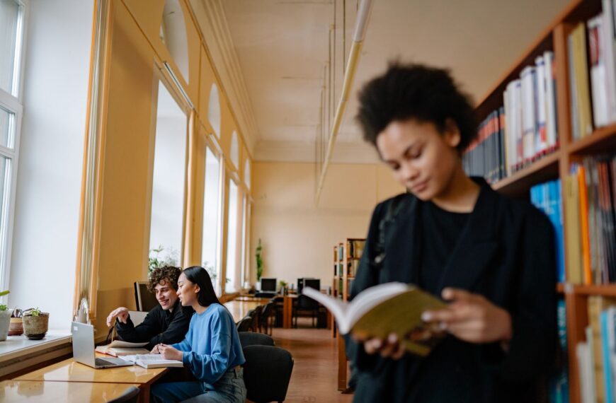 Students engaged in study sessions inside a university library, focusing on books and laptops.