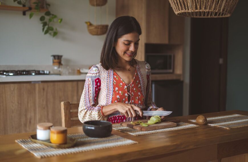 A smiling woman slices fruit on a kitchen counter, embracing a cozy and modern lifestyle.