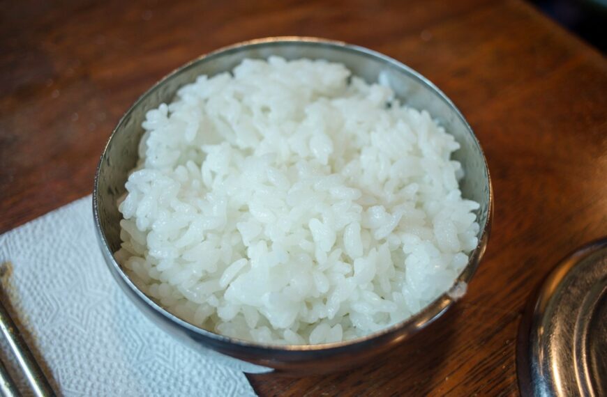 Close-up of steamed white rice in a stainless steel bowl on a wooden table.