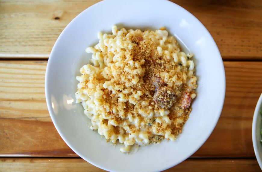 A close-up of creamy mac and cheese with breadcrumbs in a white bowl on a wooden table.