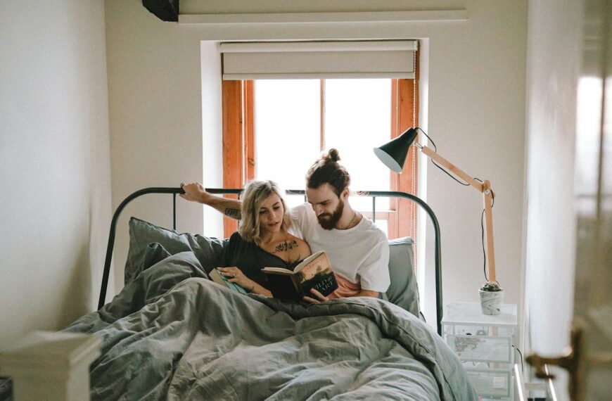 man and woman reading book on bed