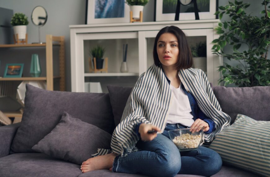 a woman sitting on a couch eating popcorn