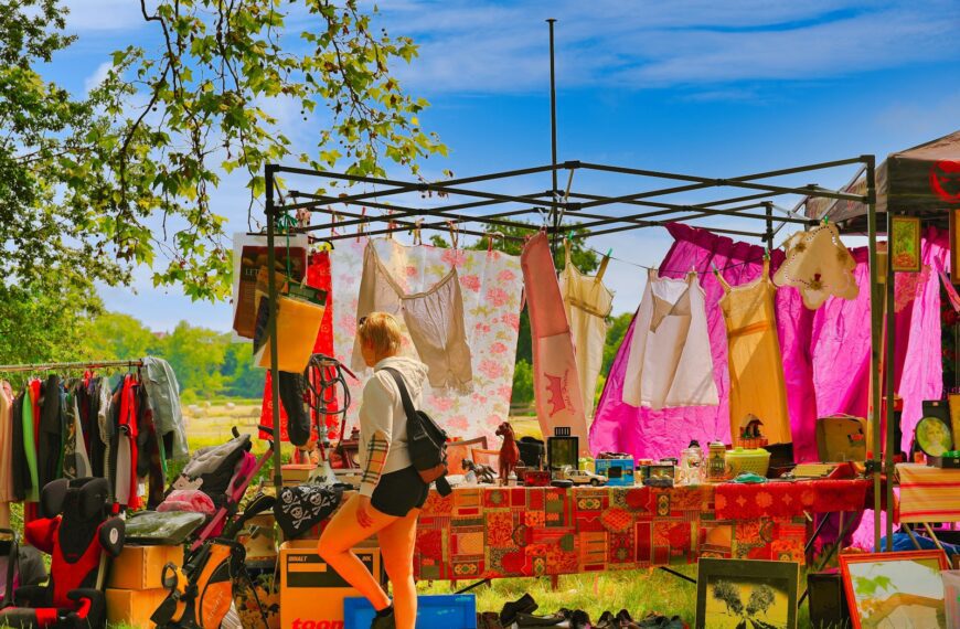 Woman browsing clothes at an outdoor market stall.
