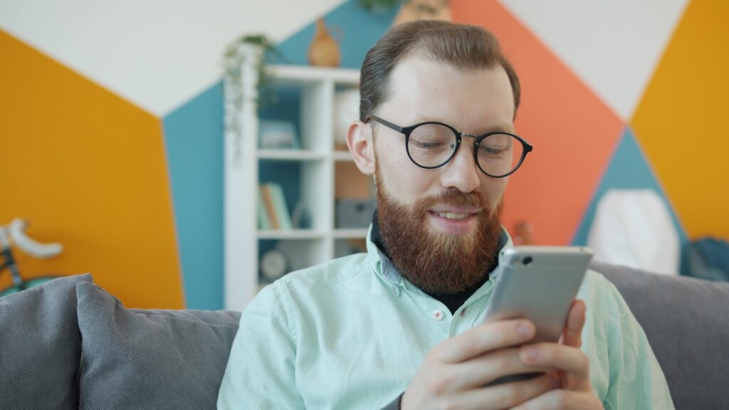 Man with beard and glasses using smartphone on smartphone.
