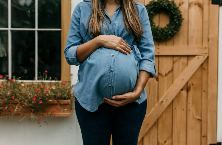 woman in blue denim button up jacket and blue denim jeans standing near brown wooden fence