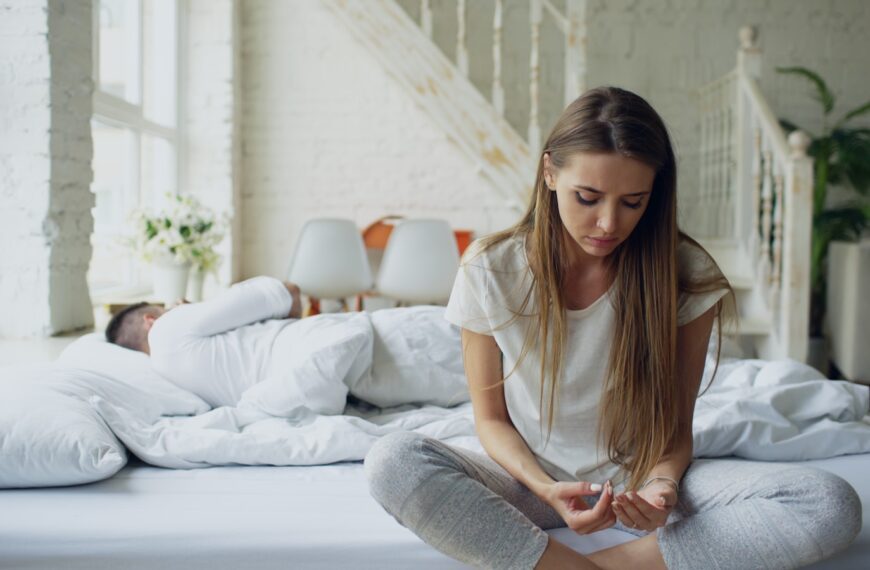 Woman sitting on bed, man sleeping behind her