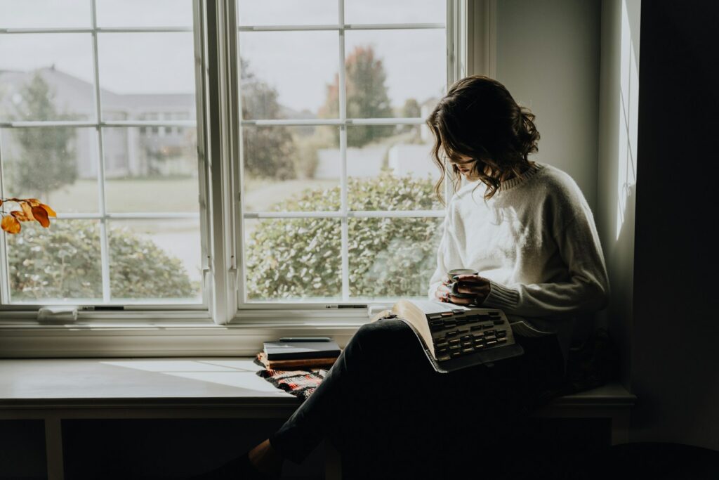 A woman sitting on a window sill reading a book