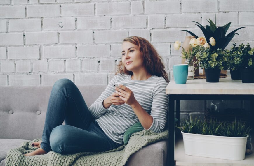 Woman relaxing on sofa with phone and coffee.