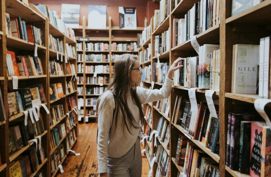 woman holding book on bookshelves