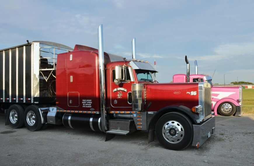 Two semi-trucks, one red and one pink, parked.