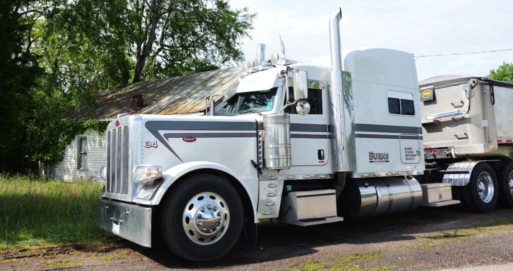 White semi-truck and trailer parked near a dilapidated house.