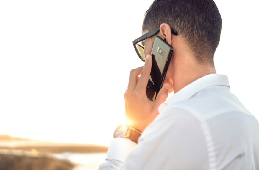 man holding smartphone standing in front of calm body of water