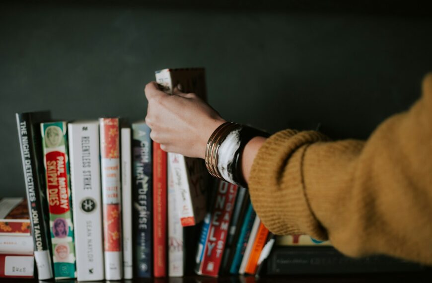 person picking white and red book on bookshelf